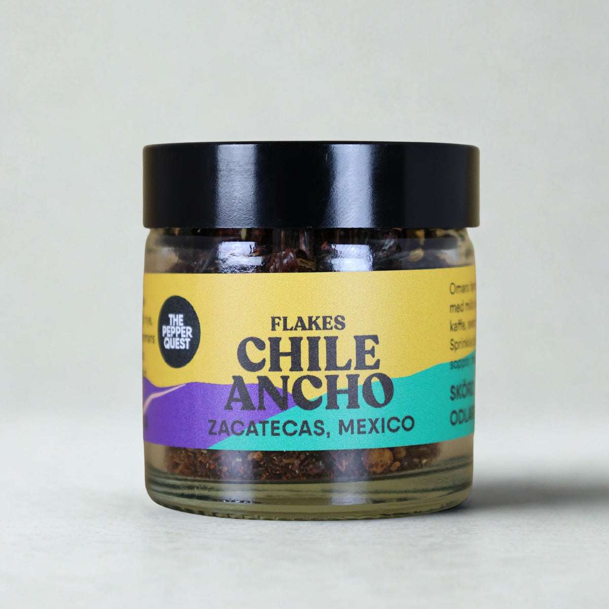 Jar of Chile Ancho flakes with a colorful label on a light gray background