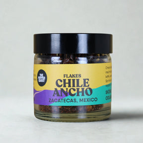 Jar of Chile Ancho flakes with a colorful label on a light gray background