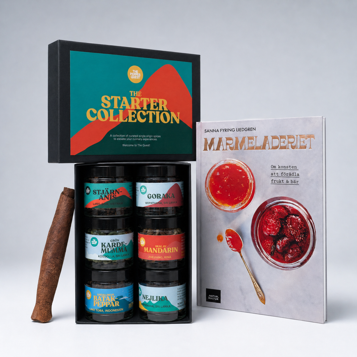 Collection of jars with labels, a cinnamon stick, and a book titled 'Marmeladeriet' on a gray background.